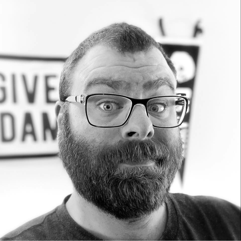 Headshot of Tyler Coderre in black and white giving a goofy look in front of a banner that says Give a Damn